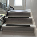 Square-edge aluminium stair nosing installed on a vinyl-covered office staircase, Premium Black anti-slip insert, viewed up the flight