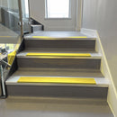 Square-edge aluminium stair nosing installed on a vinyl-covered office staircase, Yellow anti-slip insert, viewed up the flight