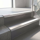Square-edge aluminium stair nosing fitted along two concrete steps in an office stairwell, with a White anti-slip insert running the full width of each step