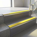Square-edge aluminium stair nosing fitted along two concrete steps in an office stairwell, with a Yellow anti-slip insert running the full width of each step