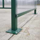 Close-up of a Moss Green smoking shelter post base plate bolted to a concrete slab with four galvanised anchors, showing the cut edge and internal flutes of the 6mm twin-wall polycarbonate panel