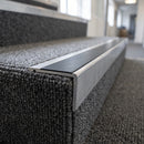 Rakeback aluminium stair nosing with black anti-slip insert on a carpeted office step, carpet tucked under the rear rib