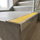 Rakeback aluminium stair nosing with yellow anti-slip insert capping a concrete step edge in a commercial stairwell