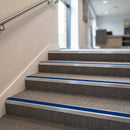 Aluminium stair nosings with cobalt blue anti-slip inserts on a grey carpeted staircase in a corporate reception