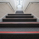 Aluminium stair nosings with red anti-slip inserts on a dark carpeted escape staircase lit by a rooflight