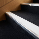 Aluminium stair nosing with a white anti-slip insert fitted to a dark charcoal carpeted hotel staircase