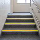Aluminium stair nosings with high-visibility yellow anti-slip inserts fitted across every step of a grey carpeted school staircase