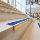 Solid brass stair nosing 59mm raked back slimline in polished brass finish with mid blue castellated anti-slip insert, fitted to a stair tread
