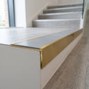 Solid brass stair nosing 59mm raked back slimline in satin brass finish with light grey smooth textured anti-slip insert, fitted to a stair tread