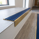 Solid brass stair nosing 59mm raked back slimline in satin brass finish with mid blue castellated anti-slip insert, fitted to a stair tread
