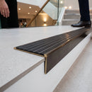 Solid brass stair nosing, 59.5mm tread with a 30mm raked-back front, in Antique Bronze finish with Black Castellated insert, fitted to a staircase