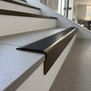 Solid brass stair nosing, 59.5mm tread with a 30mm raked-back front, in Antique Bronze finish with Black Smooth Textured insert, fitted to a staircase