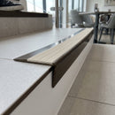 Solid brass stair nosing, 59.5mm tread with a 30mm raked-back front, in Antique Bronze finish with Porth Stone Castellated insert, fitted to a staircase