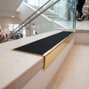 Solid brass stair nosing, 59.5mm tread with a 30mm raked-back front, in Polished Brass finish with Black Smooth Textured insert, fitted to a staircase