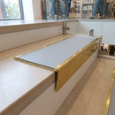 Solid brass stair nosing, 59.5mm tread with a 30mm raked-back front, in Polished Brass finish with Light Grey Smooth Textured insert, fitted to a staircase