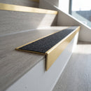 Solid brass stair nosing, 59.5mm tread with a 30mm raked-back front, in Satin Brass finish with Black Olympic Grip insert, fitted to a staircase