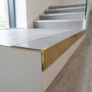 Solid brass stair nosing, 59.5mm tread with a 30mm raked-back front, in Satin Brass finish with Light Grey Smooth Textured insert, fitted to a staircase