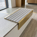 Solid brass stair nosing, 59.5mm tread with a 30mm raked-back front, in Satin Brass finish with Nimbus Castellated insert, fitted to a staircase