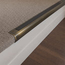 Antique Brass finish - 63.5mm solid brass bullnose stair nosing fitted to a carpeted step, aged olive-brown brass with a black anti-slip insert