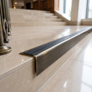 Solid brass stair nosing 71mm raked back in antique brass with black castellated insert fitted on a porcelain tiled hotel lobby staircase