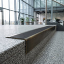 Solid brass stair nosing 71mm raked back in antique brass with black smooth textured insert fitted on a granite atrium staircase