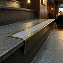 Solid brass stair nosing 71mm raked back in antique brass with flint castellated insert fitted on a slate restaurant staircase