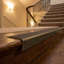 Solid brass stair nosing 71mm raked back in antique brass with peat castellated insert fitted on a dark oak hotel stairwell