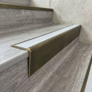 Solid brass stair nosing 71mm raked back in antique brass with polar grey smooth textured insert fitted on a vinyl plank school staircase