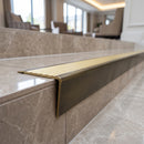 Solid brass stair nosing 71mm raked back in antique brass with satin brass insert fitted on a porcelain tiled hotel lobby staircase