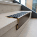 Solid brass stair nosing 71mm raked back in antique bronze with black castellated insert fitted on a porcelain tiled hotel lobby staircase