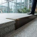 Solid brass stair nosing 71mm raked back in antique bronze with polar grey castellated insert fitted on a porcelain tiled hotel lobby staircase