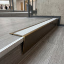 Solid brass stair nosing 71mm raked back in antique bronze with polar grey smooth textured insert fitted on a vinyl plank school staircase