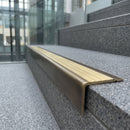 Solid brass stair nosing 71mm raked back in antique bronze with satin brass insert fitted on a porcelain tiled hotel lobby staircase