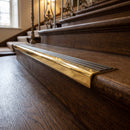 Solid brass stair nosing 71mm raked back in polished brass with antique bronze insert fitted on a dark oak hotel stairwell