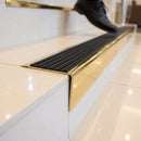 Solid brass stair nosing 71mm raked back in polished brass with black castellated insert fitted on a porcelain tiled hotel lobby staircase