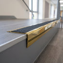 Solid brass stair nosing 71mm raked back in polished brass with black olympic grip insert fitted on a vinyl plank school staircase