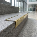 Solid brass stair nosing 71mm raked back in polished brass with light grey castellated insert fitted on a granite atrium staircase
