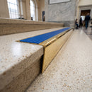 Solid brass stair nosing 71mm raked back in polished brass with mid blue castellated insert fitted on a terrazzo museum foyer staircase