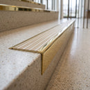 Solid brass stair nosing 71mm raked back in polished brass with porth stone castellated insert fitted on a terrazzo museum foyer staircase