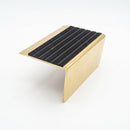 Solid brass stair nosing 71mm raked back single channel in polished brass with black castellated insert on a white studio background