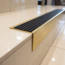 Solid brass stair nosing 71mm raked back in satin brass with black castellated insert fitted on a porcelain tiled hotel lobby staircase