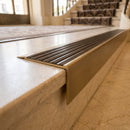 Solid Brass Stair Nosing 71mm Tread Square Front Slimline in Antique Brass finish with Antique Bronze insert fitted on a hotel lobby staircase with cream marble treads
