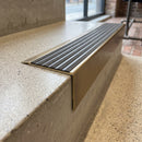 Solid Brass Stair Nosing 71mm Tread Square Front Slimline in Antique Brass finish with Granite Castellated insert fitted on a retail store staircase with polished concrete treads