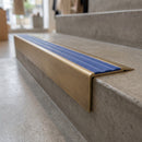 Solid Brass Stair Nosing 71mm Tread Square Front Slimline in Antique Brass finish with Mid Blue Castellated insert fitted on a retail store staircase with polished concrete treads