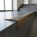 Solid Brass Stair Nosing 71mm Tread Square Front Slimline in Antique Brass finish with Polar Grey Castellated insert fitted on a public building staircase with dark stone treads