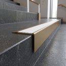 Solid Brass Stair Nosing 71mm Tread Square Front Slimline in Antique Brass finish with White Castellated insert fitted on a public building staircase with dark stone treads
