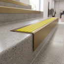 Solid Brass Stair Nosing 71mm Tread Square Front Slimline in Antique Brass finish with Yellow Castellated insert fitted on a retail store staircase with polished concrete treads