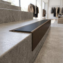 Solid Brass Stair Nosing 71mm Tread Square Front Slimline in Antique Bronze finish with Black Smooth Textured insert fitted on a retail store staircase with polished concrete treads