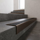 Solid Brass Stair Nosing 71mm Tread Square Front Slimline in Antique Bronze finish with Black Olympic Grip insert fitted on a public building staircase with dark stone treads