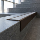 Solid Brass Stair Nosing 71mm Tread Square Front Slimline in Antique Bronze finish with Light Grey Smooth Textured insert fitted on a public building staircase with dark stone treads